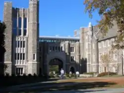 Four-story tower on left with an arched walkway in the center and pedestrian bridge connecting the tower to three-story Gothic building