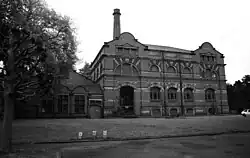 Black and white image of an ornate Edwardian brick building with high facade and a tall chimney against a pale sky