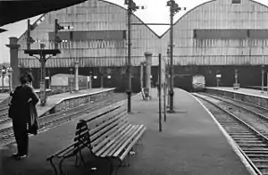 A black and white image of railway lines and platforms with two overall shed roofs covering the station