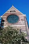 The liturgical west (actually south) end of the church, showing the steep roof surmounted by a small cross and the rose window below.