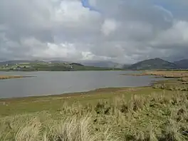 A view of Broad Water with grass in the foreground leading down to the shore , and hills in the background behind the lake.