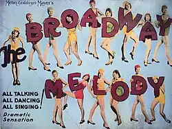 Movie poster featuring fifteen young women in dance outfits. The first appears to hold the word "The" in large letters. The other fourteen hold up the individual letters that spell out "Broadway Melody". Accompanying text reads, "All Talking, All Dancing, All Singing! Dramatic Sensation."