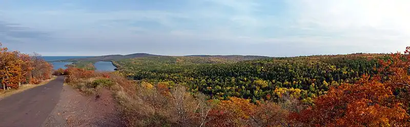 An autumnal panorama from the top of Brockway Mountain with Lake Fanny Hooe and Lake Superior in the distance and Brockway Mountain Drive descending the hill.