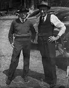 Black and white photo of two men standing outdoors in a forested area