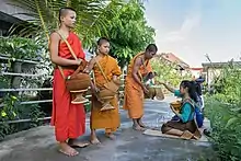 Buddhist alms in Don Det. Every day, early morning three child monks from the temple walk in the village with their alms bowls to collect food, prepared and offered by the locals, and to recite a short prayer in exchange. Ritually, Buddhist monks in Laos have only two meals a day: one in the morning and one at noon. They fast in the evening.