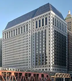 A rectangular building with a sloped black glass roof is seen from across the river to the northwest