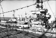 Two large ships bristling with guns moored close to shore.