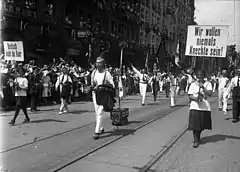 People holding banners and waving flags march down a street. Lining the road are crowds of supporting people.