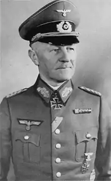 A man wearing a peaked cap, military uniform with an Iron Cross displayed at the front of his uniform collar.