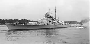 A black-and-white photograph of a warship positioned 45 degrees to the left of the viewer, bow first