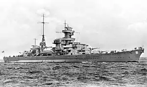 A large gray warship cruising through calm seas; several men are standing on the deck