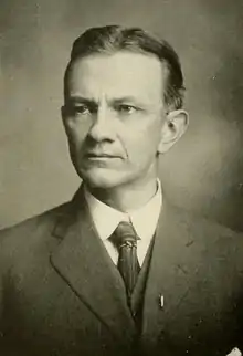 Head and shoulders photograph of a man in a Victorian suit.  He has a beard, a large mustache and is slightly balding.  He wears a serious expression and is looking slightly to the right.