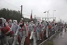 Photo of a group of people in translucent white coveralls walking down a large road.