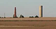 Tall brick chimney and cylindrical concrete water-tower standing alone in cornfield