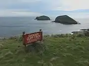 Cliff warning sign at Cape Grim, Tasmania, with The Doughboys in the background