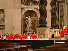 The cardinals, all in bright red robes, are grouped near the baldachin.