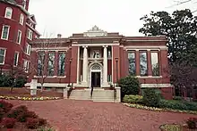 A one-story brick building with grey concrete stairs in the center leading to a door with a column on either side of it. There are three long windows on each side of the building.