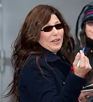 Image of Catherine Keener head and torso. She is wearing a heavy coat and dark sunglasses. Keener is holding a blue sharpie and appears to be signing autographs.