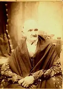 Katharine Smith Salisbury sometime before 1893. She is visibly aged. She wears a dark shawl over a long-sleeved top (likely a dress) and sits in an ornate wooden chair. Her expression is firm.