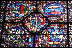 Part of a large window. It is divided into four circular panels with a quatrefoil (or four-lobed section) between them and an arched segment beneath. To the lower right, a knight, Sagittarius, is being welcomed home. At the centre a man empties a water pot, symbolising Aquarius and a two-faced figure symbolises New Year. To the upper right, are the two fish of Pisces. The other sections show each month's activities: grapevine pruning, bell-ringing and sitting by the fire.