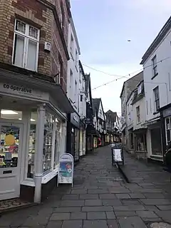 Street scene. Buildings lining narrow lane with central water gully, pedestrians (2018)