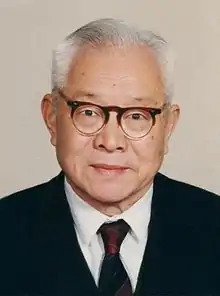 Colour photograph of Chi-Ming Chu, an elderly man wearing glasses and a tie and jacket.