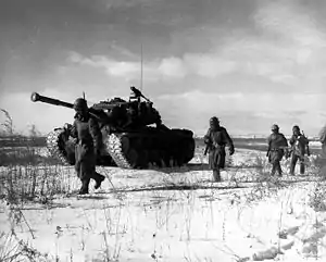 Men advancing through the snow with a tank