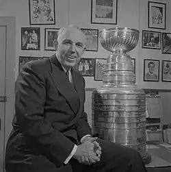 Campbell wearing a suit and tie, sitting on a desk with the Stanley Cup