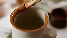  Application of an iron-rich clay slip (clay-paint) on the clay body of a skyphos, before firing. Contemporary black glaze pottery production (Athens).