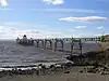 Metal pier standing on thin legs rising from the sea. Beach in the foreground