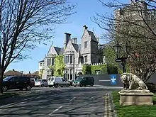 Long shot view of Clontarf Castle from a side angle. Clontarf Castle is a grey castle. There are leafless trees in the foreground. The sky is blue and clear.