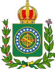 Coat of arms consisting of a shield with a green field with a golden armillary sphere superimposed on the red and white Cross of the Order of Christ, surrounded by a blue band with 20 silver stars; the bearers are two arms of a wreath, with a coffee branch on the left and a flowering tobacco branch on the right; and above the shield is an arched golden and jeweled crown.