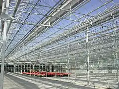 Modern gutter-connected glass greenhouse with open roof ventilation and concrete floors