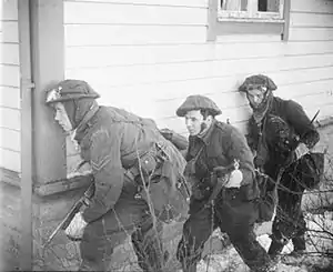 three British soldiers take cover at the corner of a house