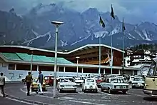 External view of stadium with snow-capped mountains in the background and cars in a parking lot in the foreground