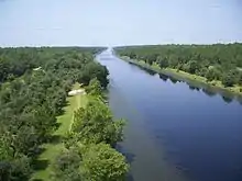 View down on a canal approximately 100 feet across disappearing into the horizon, bordered by trees