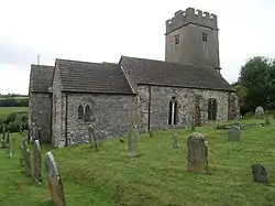 Stone building with square tower. In the foreground are gravestones.