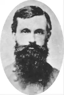 Black and white oval-shaped photo of a man with a heavy, dark beard.