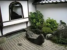 A wall with window and a raked stone garden.