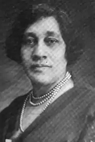 A middle-aged African-American woman, hair cropped to chin length, wearing a dress with a surplice neckline and pearls