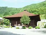 Wooden building with a hipped roof and an enclosing veranda without handrails.