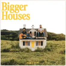 Dan and Shay sitting on the roof of a model house in the middle of a field