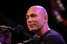 close-up of Daniel Landa in front of a microphone, looking left of camera with slight smile