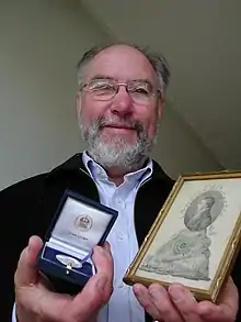 Photograph of David Galloway holding the Acharius Medal 2008 and a picture of Erik Acharius