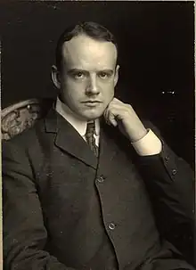 A slightly balding white man in a formal suit, seated, his head resting on his left hand