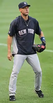 A man in a navy windbreaker and navy hat prepares to catch a baseball.