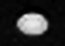 A white oval shaped object somewhat elongated horizontally is seen in the center. There are a few small dark spots on its surface.