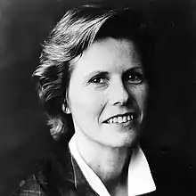 A professional black-and-white headshot of a smiling white woman with short blond hair.