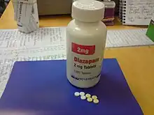 White bottle with red and black labels on a blue pad atop a desk. Also on the pad are seven small pills.