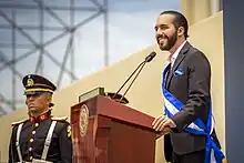 A man (Nayib Bukele) standing at a podium and speaking to a large crowd.